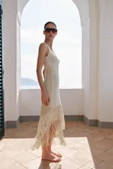 Vestido midi de escote redondo y sin mangas, confeccionado en tejido con textura. Presenta un diseño recto con bajo acabado en capas de flecos largos al tono.