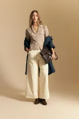 Top de tejido color beige claro, manga corta, escote en V con cierre frontal de botones y ribetes negros en el cuello y el borde del escote.