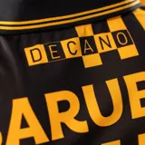 Camiseta de fútbol Puma del Club Atlético Peñarol, edición aniversario, modelo de manga larga. Diseño con mitad derecha a rayas verticales amarillas y negras, y mitad izquierda negra con escudo del CURCC y logo de Puma en dorado. Presenta cuello polo negro y sponsor antel en el pecho.