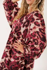 Vestido midi con estampado animal print en tonos borgoña y beige, con escote redondo y abertura en el pecho que se ajusta con lazos finos. De silueta relajada, manga larga tipo globo con terminación fruncida y falda amplia con recortes.