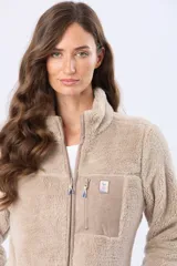 Campera de sherpa color beige con cuello alto y cierre frontal. Presenta un bolsillo frontal en el pecho de gamuza color arena con cierre y etiqueta decorativa, además de detalles en gamuza en los bordes.