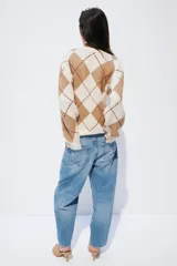 Saco tipo cárdigan de punto jacquard con diseño de rombos, escote en pico, cierre frontal con botones y hombros caídos. Presenta terminaciones acanaladas en cuello, puños y ruedo.