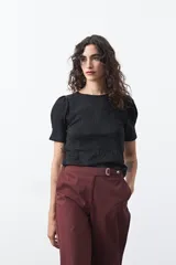 Remera negra de manga corta con textura floral en relieve. Presenta un diseño de inspiración romántica con mangas ligeramente abullonadas que aportan estructura y un ajuste al cuerpo.