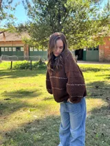 Buzo de tejido de punto en color marrón chocolate, con diseño oversize, cuello redondo y mangas largas abullonadas. Presenta detalles de líneas horizontales en color crudo y terminaciones en contraste en cuello, puños y ruedo.