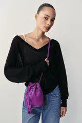 Mini bandolera de piel color morado, de diseño tipo saco con cierre fruncido y cordón ajustable con borlas en el extremo. Cuenta con asa larga ajustable y detalles metálicos dorados.
