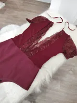 Body de lycra color bordó con mangas cortas de encaje y detalle de encaje vertical en el frente. Presenta un diseño con espalda descubierta y tiras finas para atar en el cuello.