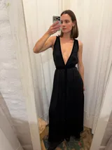 Vestido largo de seda color bronce con acabado brillante, escote profundo en V y espalda abierta. Presenta detalles en terciopelo negro que enmarcan el escote, recorren el frente y definen la cintura con una faja ajustable. Posee breteles anchos y una abertura frontal en la falda.