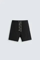 Bermuda negra de corte regular, confeccionada en tejido jacquard con efecto arrugado. Presenta cintura elástica ajustable con cordón blanco, bolsillos laterales y bolsillos traseros de vivo.