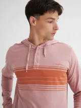 Remera manga larga color beige con capucha y media cartera de botones. Presenta bolsillo tipo canguro y rayas horizontales en el pecho en color marrón.