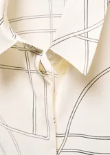 Camisa de corte recto y tejido fluido, con cuello camisero, cierre frontal de botones y mangas largas con puños abotonados. Presenta un estampado geométrico lineal sobre fondo color crema.