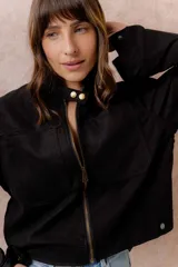 Chaqueta de gamuza sintética color negro, de calce relajado y largo a la cintura. Presenta cuello mao con cierre a presión, cierre frontal metálico, bolsillos delanteros de placa y puños con broche regulable.