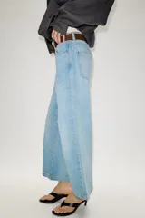 Jeans de tiro alto con pernera ancha y corte cropped. Presenta diseño de cinco bolsillos, cierre frontal con cremallera y botón, e incluye un cinturón de gamuza marrón con hebilla metálica.