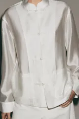Camisa de estilo oriental confeccionada en mezcla de lyocell con acabado satinado. Presenta cuello redondo, manga larga con puños rectos, bolsillos de plastrón y cierre frontal mediante alamares.