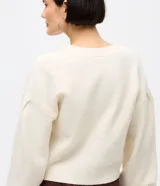 Cardigan de punto color crema con escote en V, cierre frontal de botones y mangas largas abullonadas con puños acanalados. Presenta un diseño corto y ajuste cómodo.