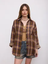 Camisa de flanela a cuadros en tonos marrones y azules, de corte oversize, con mangas largas y bolsillos frontales.