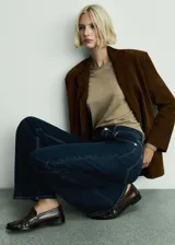 Pantalón jeans de tiro alto con diseño acampanado, confeccionado en tejido de algodón con un ligero toque de elastano. Presenta un lavado oscuro tipo rinse, cierre frontal con cremallera y botón, y cuenta con cinco bolsillos.