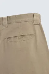 Pantalón chino de corte baggy fit, confeccionado en tejido de algodón. Presenta perneras amplias y holgadas, bolsillos frontales y traseros, con cierre de cremallera y botón.