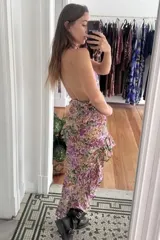 Vestido midi con diseño asimétrico, escote halter con tiras ajustables y espalda descubierta. Presenta un estampado floral multicolor y falda con volados en el ruedo.