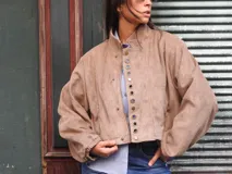 Campera bomber color beige, de corte oversize, con cuello redondo, cierre frontal de broches y mangas abullonadas.