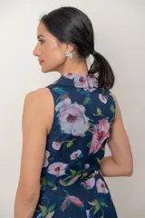 Vestido midi de organza azul marino con estampa floral en tonos rosados y verdes. Presenta escote en V cruzado con solapas, sin mangas, falda evasé de capas asimétricas y estructuradas.