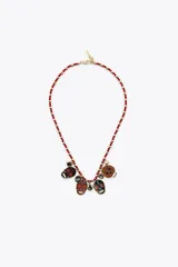 Pack de dos collares. El primero es una cadena doble con abalorios rojos y eslabones dorados, adornado con varios dijes de calaveras esmaltadas con detalles coloridos y piedras oscuras. El segundo collar es una cadena dorada más larga con un dije colgante de corazón esmaltado con motivos florales y un dije en forma de signo de interrogación.