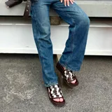 Zueco de mujer con plataforma y taco bajo, color marrón oscuro. La capellada es de tiras trenzadas en patrón damero (cuadros) en tonos marrón oscuro y blanco/beige.