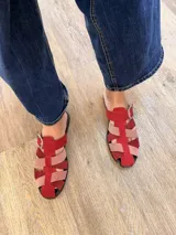 Suecos tipo sandalias franciscanas elaborados en cuero, con tiras entrelazadas de gamuza en tonos rojo, rosado y bordó. Cuentan con una hebilla metálica lateral y suela plana.