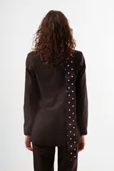 Blazer negro de corte clásico, con solapas de muesca, cierre frontal de un solo botón y bolsillos de ojal. Se combina con un pañuelo de seda azul marino con lunares blancos anudado al cuello.