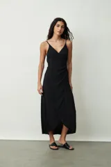Vestido negro midi de tirantes finos, con escote cruzado en V y diseño envolvente con drapeado lateral que genera una abertura frontal.