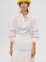 Falda larga blanca confeccionada en broderie de algodón con diseño de paneles escalonados, detalles de galones con transparencias en color azul y naranja, y pretina elástica con cordón ajustable.