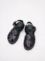 Sandalias de cuero marrón con tiras entrecruzadas, suela de goma negra con pespuntes blancos y hebilla lateral.