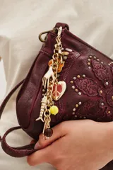 Llavero decorativo para bolso con cadena de eslabones dorados y múltiples dijes colgantes, incluyendo una mano, un corazón con símbolo de paz, un pez y cuentas de vidrio de colores.