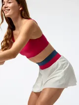 Skort deportivo blanco con pretina ancha tejida en colores fucsia y azul. Cuenta con short incorporado en el interior y diseño plisado central, inspirado en el estilo de tenis vintage.