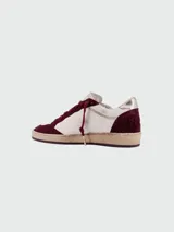 Zapatillas de estilo urbano con diseño desgastado, combinan paneles de cuero blanco y gamuza en color bordó. Presentan una estrella lateral con acabado brillante, cordones al tono y suela de goma con efecto envejecido.