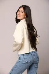 Buzo tejido de punto en color blanco crema, con cuello redondo alto y mangas largas con puños acanalados.