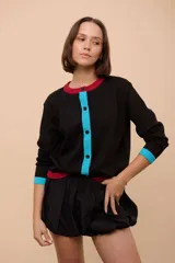 Cárdigan negro de punto con cuello redondo, cierre frontal con botones celestes y ribetes en cuello y puños de color rojo.