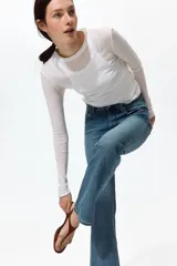 Jean de tiro alto y corte bootcut, confeccionado en denim de algodón levemente elástico con lavado azul medio y efecto desgastado. Presenta diseño clásico de cinco bolsillos, cierre de cremallera y botón metálico.