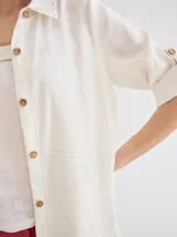 Vestido camisero midi de lino color beige, con diseño de manga corta con solapa, cuello camisero, bolsillo trasero con solapa y botón, y aberturas laterales en el ruedo.
