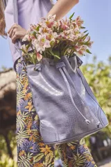 Bolso tipo bucket color celeste con textura simil cuero de cocodrilo, cierre con cordón ajustable, correa de hombro ajustable y asa de mano.