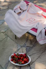 Buzo color crema con cuello polo, mangas largas y puños ajustados. Presenta un bolsillo en el pecho con bordados de frutas y la inscripción "Bom Faro by Coppelia". Los bordes del cuello, el bolsillo y los puños están decorados con puntadas rojas.