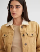 Campera de gabardina color mostaza, forrada con corderito color crudo en el cuerpo y cuello. Tiene corte clásico y botones metálicos personalizados.