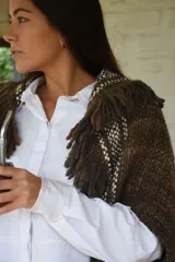 Capita artesanal de lana merino pura, color marrón con textura tejida y flecos decorativos en los bordes.