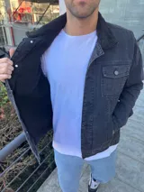 Chaqueta de jean color negro con cuello de corderito negro, cierre frontal con botones metálicos y bolsillos frontales con solapa.
