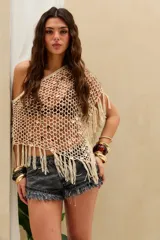 Top corto tejido en crochet de color crudo, con diseño de red adornado con lentejuelas y flecos colgantes en el dobladillo. Presenta un corte asimétrico de un solo hombro.