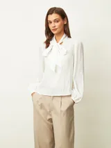 Blusa de textura arrugada con cuello alto y lazo frontal para anudar. Presenta mangas largas con puños elásticos y corte recto.