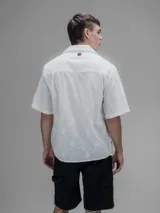 Camisa blanca de manga corta, con cuello abierto y calce oversize. Confeccionada en algodón bordado tipo broderie con diseño floral.