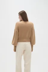Saco de punto color beige, con cuello redondo, cierre frontal con botones y mangas largas con puños acanalados.