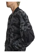 Campera tipo bomber de malla ligera con estampado camuflado en tonos grises y negros. Presenta cierre frontal, cuello, puños y bajo acanalados, además de un bolsillo con cremallera en la manga izquierda.