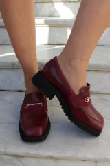 Mocasín de cuero vacuno color bordó con suela track negra de goma. Presenta un diseño de punta cuadrada con un herraje metálico plateado sobre una banda de gamuza en la capellada.