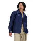 Campera azul marino estilo entrenador, con cierre de botones a presión, cuello clásico y dos bolsillos frontales. Logo de New Balance bordado en blanco en el pecho y parche decorativo en la espalda. Puños con tres rayas blancas.